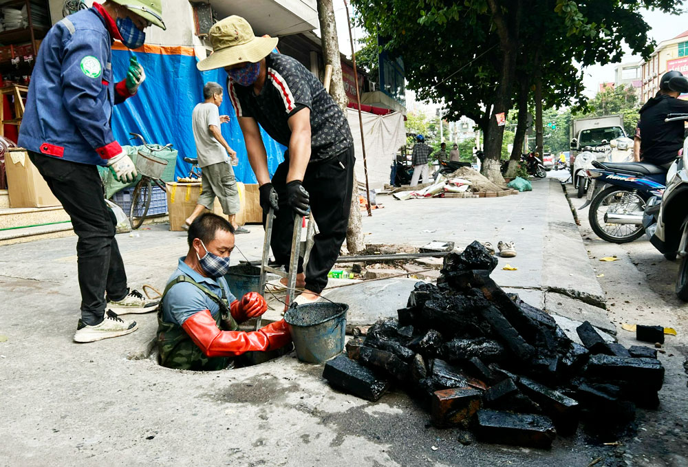 Ảnh: Công nhân lắp quả lô chuyên dụng vào dây cáp để nạo vét rác thải trong hố ga trên đường Quang Trung.